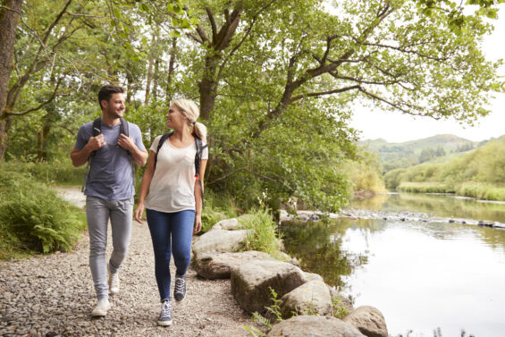 A young man and woman hike through woods beside a lake.