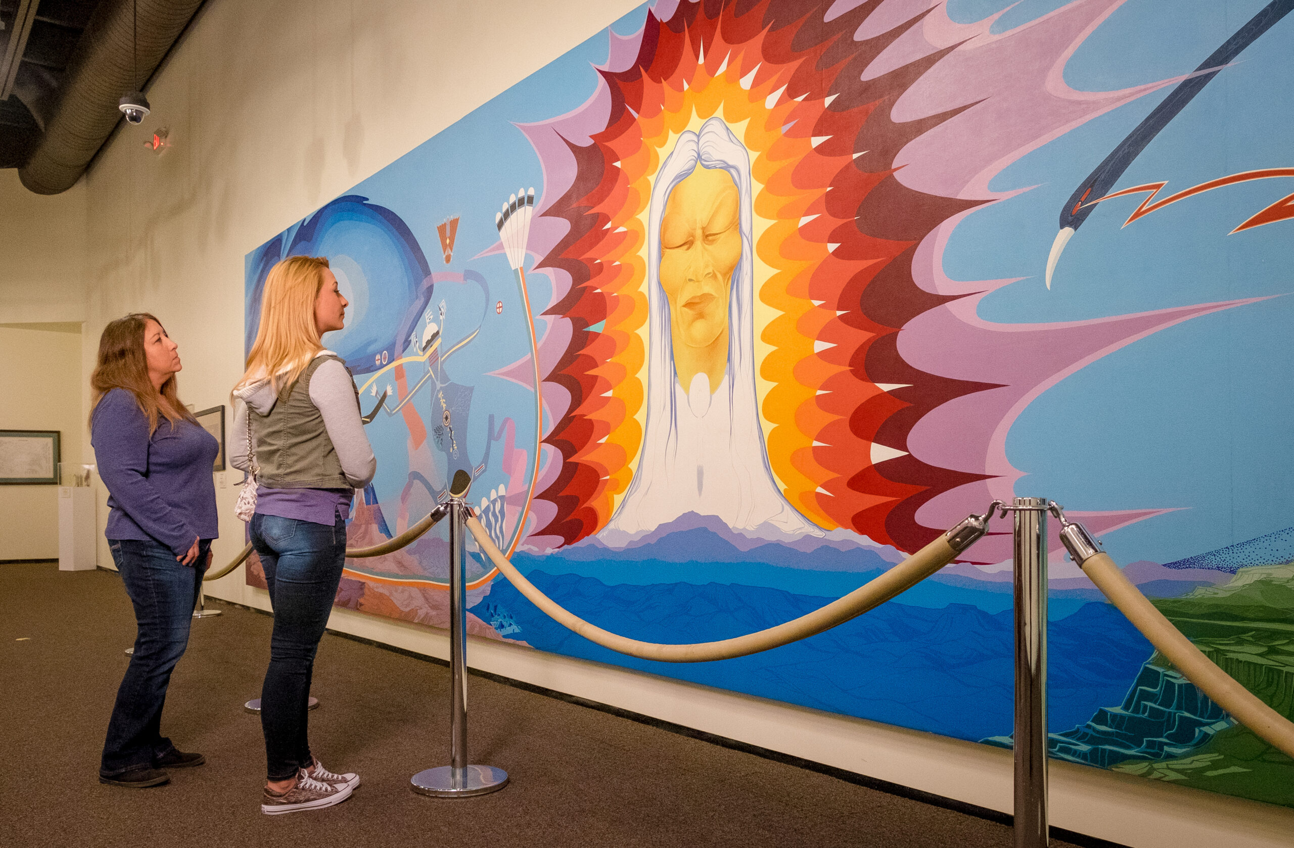 Two young women observe a colorful painting at a museum in Wichita.
