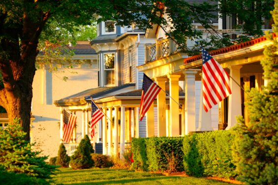 Two and three-story colonial style homes with American flags hanging out front at sunset.