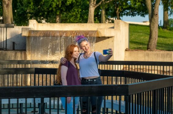 Two friends smile for a selfie at sunset in front of a concrete fountain.