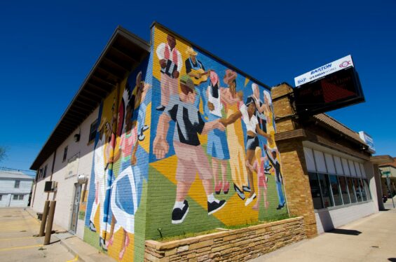 Colorful Art Deco mural of people dancing and playing music on a store corner.