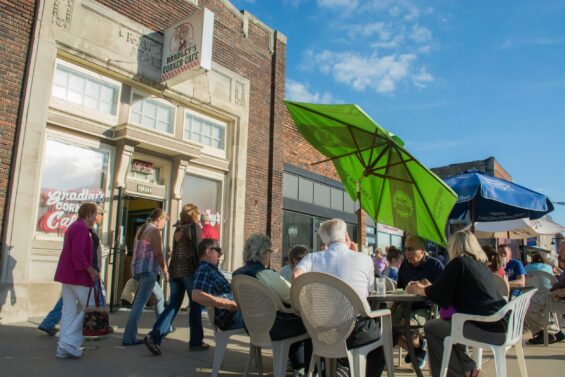 Groups of people sit outside the brick Bradley's corner cafe under colorful umbrellas.
