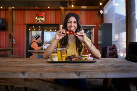 Woman smiles holding a rib in a western-looking restaurant.